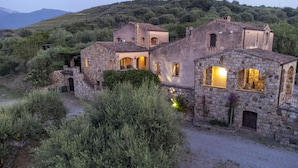 Un edificio de piedra con varias habitaciones, rodeado de vegetación y colinas.