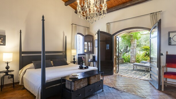 Una cama con dosel, una mesita de noche, un candelabro y vistas a un patio exterior con un banco.