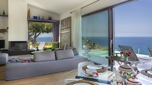 A modern living room with a sofa, dining table, and a view of the sea.