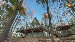 A rustic cabin with a wooden deck and stairs leading to the entrance. - The Lookout | Secluded A-Frame | Hot Tub | Games (Campton)