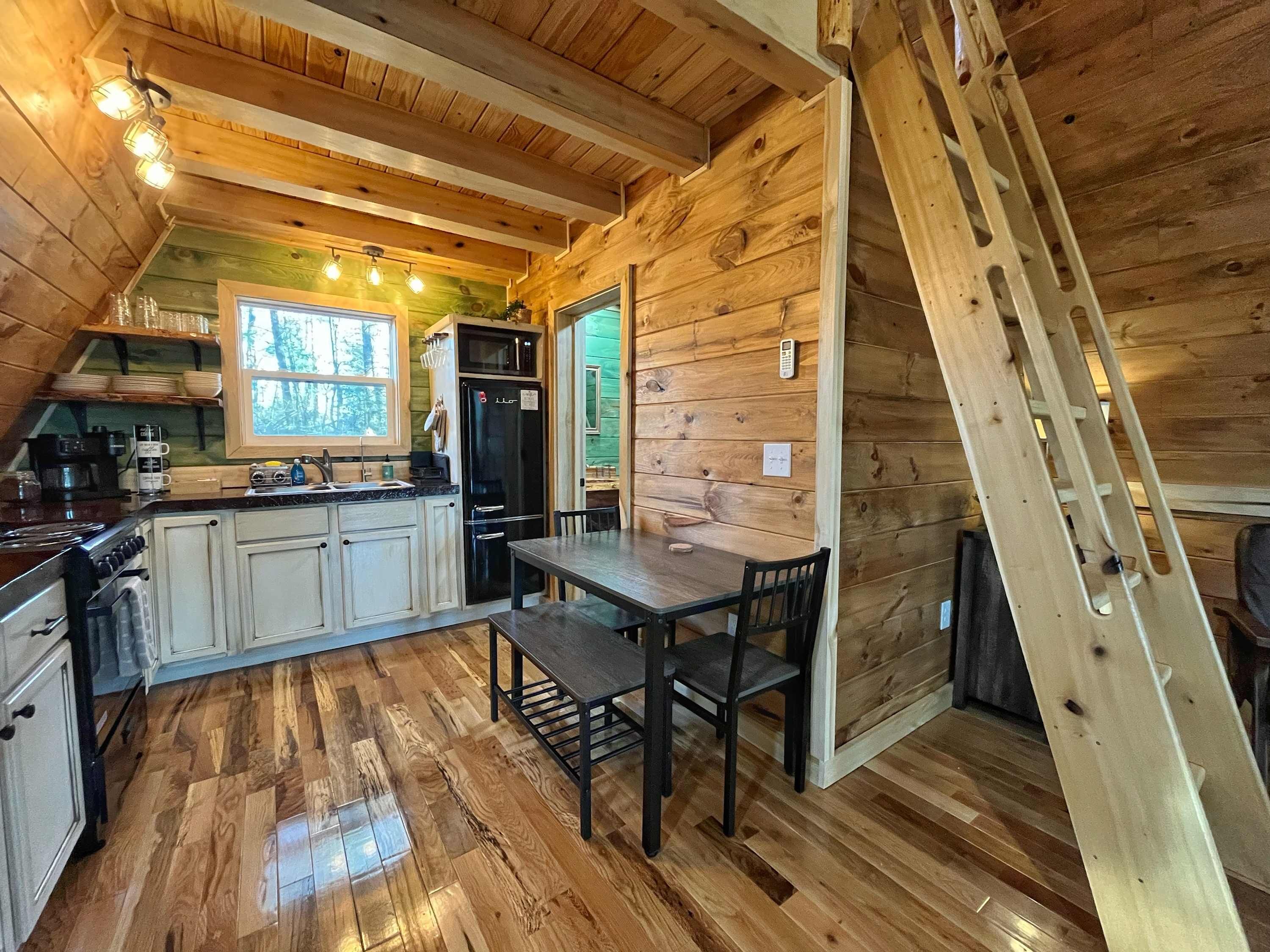 A wooden cabin interior with a kitchen, dining area, and a ladder.