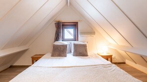 A cozy attic bedroom with a sloped ceiling, a window with curtains, a bed with a white quilt, and a bedside lamp. - Lovely apartment in villa for 6 people with WIFI and TV (Bruges)