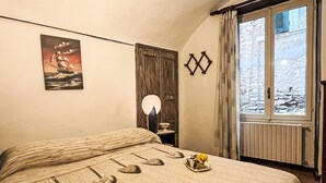 Een slaapkamer met een bed, een nachtkastje met lamp, een raam met uitzicht en een schilderij aan de muur.