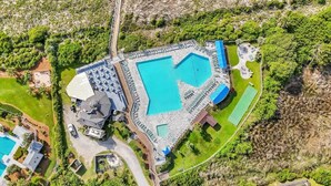 Vista aèria d'un complex turístic amb una gran piscina central, nombroses habitacions i vegetació abundant al voltant.