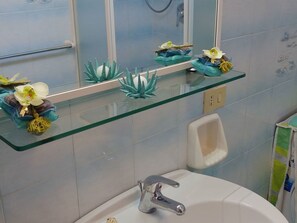 Ein Badezimmer mit einer Glastrennwand, einem Waschbecken mit Chromarmatur und einem Urinal.