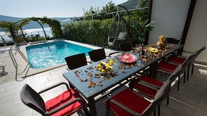 Un espacio de comedor al aire libre con piscina, sillas de mimbre y una mesa lista para una comida.