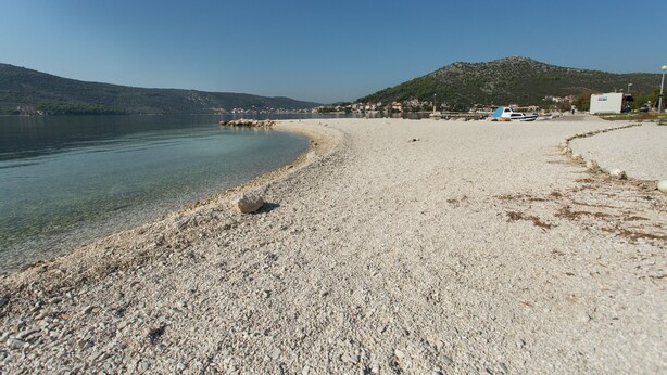 Una playa de guijarros con barcos y una colina al fondo.