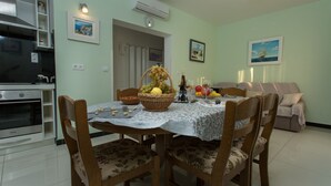 Un comedor con una mesa dispuesta para cuatro, rodeada de sillas de madera con tapicería floral. Una cesta de mimbre con fruta y una botella de vino están sobre la mesa.