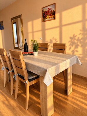 A dining room with a rectangular table, wooden chairs, a vase with flowers, a bottle, and a framed picture on the wall. - Apartment Bodulo 2 (Povljana)