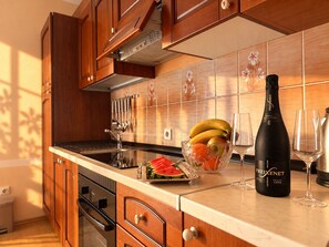 A kitchen with wooden cabinets, a stainless steel range hood, a fruit bowl with bananas and watermelon, and a bottle of Freixenet Cava wine.