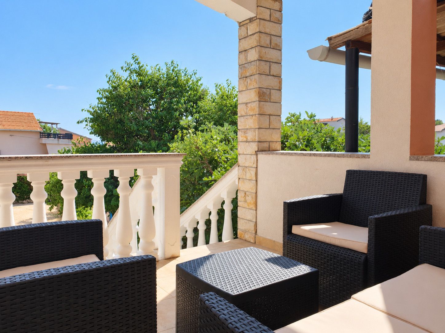 Une terrasse extérieure avec des meubles en osier et une balustrade blanche.