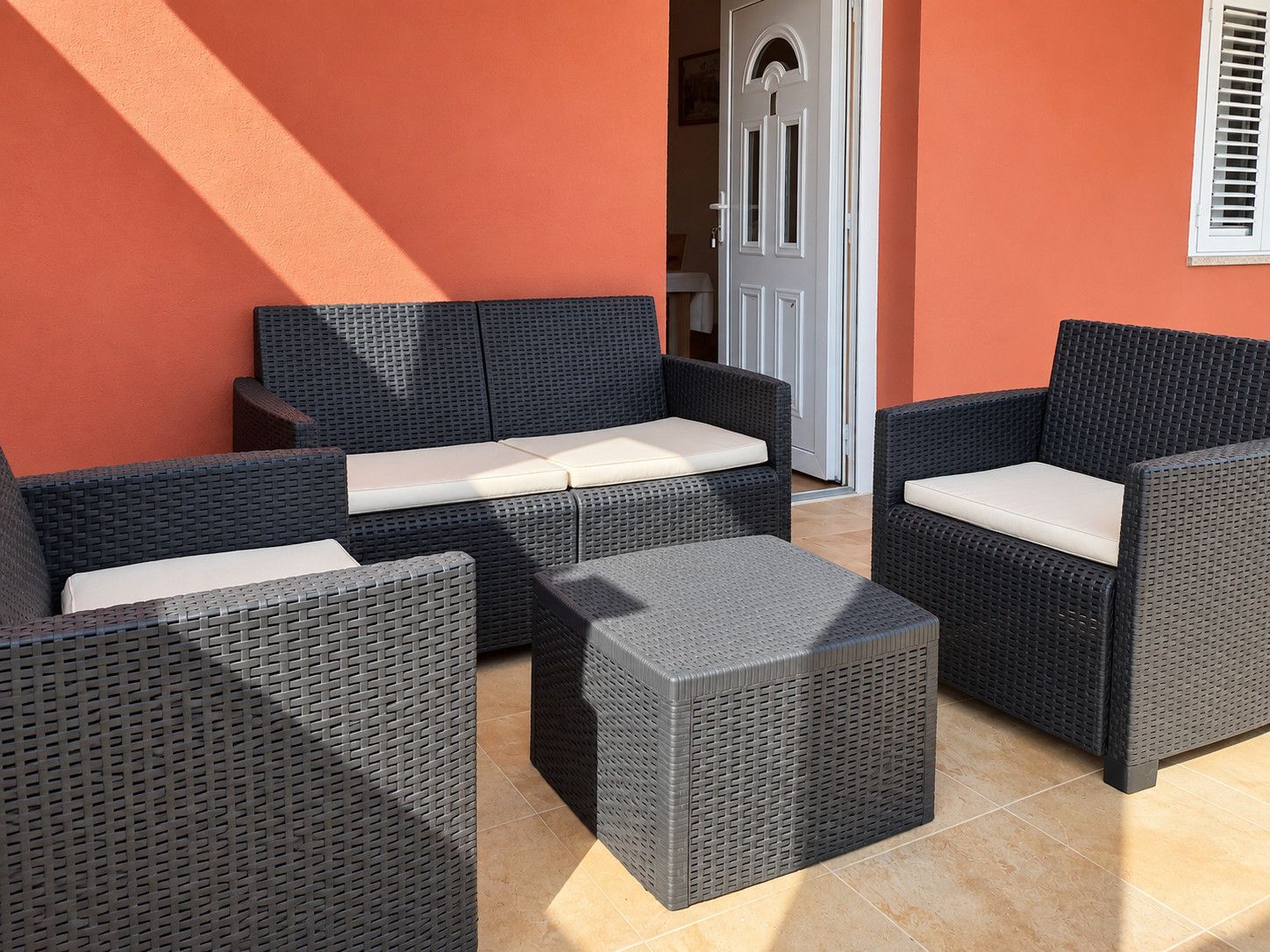 Un área de patio con mobiliario de mimbre, incluyendo un sofá y dos sillones, y una mesita.