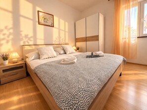 A modern bedroom with a large bed, a bedside table with a lamp, a small plant, and a framed picture on the wall.