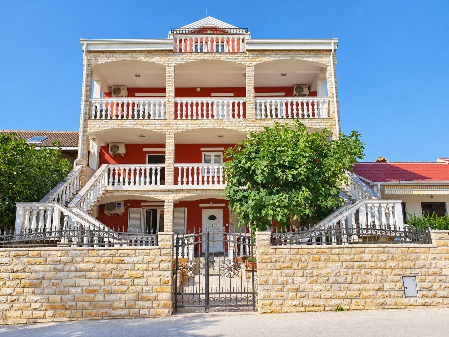 Um edifício de vários andares com varandas, uma parede de pedra e um portão.
