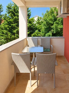 A balcony with wicker furniture, a table, and a view of trees and a building.