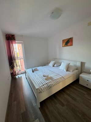 Un dormitorio con cama, mesita de noche, un cuadro en la pared y una ventana con cortinas.
