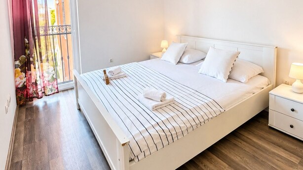 Una habitación de hotel con cama, mesitas de noche, una ventana con cortinas y un cuadro en la pared.
