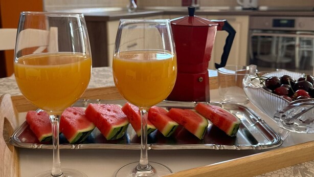 Un plateau de petit-déjeuner avec deux verres de jus d’orange, des tranches de pastèque et un bol de raisins, posé sur une table dans une cuisine.