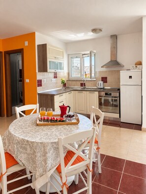 A modern kitchen with white cabinets, a stainless steel range hood, and a dining area with a round table and white chairs.