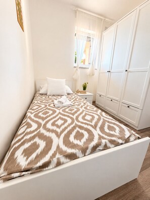 A bedroom with a bed, white wardrobe, and a window with curtains.