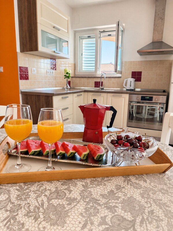 A breakfast tray with watermelon slices, cherries, and orange juice glasses on a table in a kitchen with a tiled backsplash and a window.