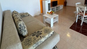 Un salon comprenant un canapé, une table basse, un téléviseur et un coin repas avec des chaises et une table.