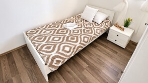 Un dormitorio con cama, mesita de noche, una obra de arte en la pared y una ventana con cortinas.