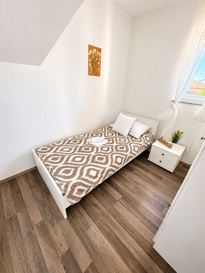 Quarto com cama, mesa de cabeceira, um quadro na parede e janela com cortinas.