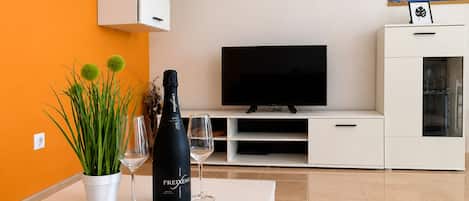 Ett modernt vardagsrum med en platt-TV, ett vitt skåp och ett bord med en flaska och glas.