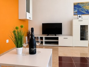 Uma sala de estar moderna com televisão de tela plana, um armário branco e uma mesa com garrafa e copos.