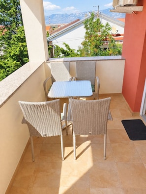A balcony with a table and chairs, a view of buildings and mountains, and a red wall.