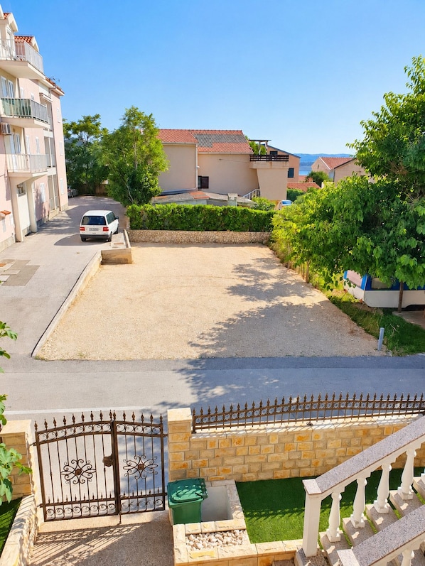 A residential area with a paved driveway, a gated entrance, and a small garden area with a green container and a white bench.