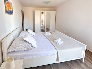 A single-bed room with a wardrobe, a mirror, and a bedside table with a lamp.