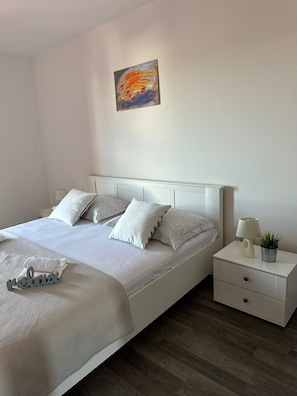 Un dormitorio ordenado con cama, almohadas, mesita de noche con lámpara y una planta pequeña.