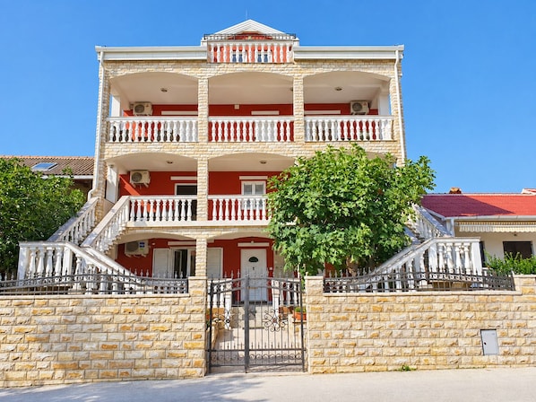 Um edifício de vários andares com varandas, uma parede de pedra e um portão.