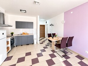 A modern kitchen with grey cabinets, a white refrigerator, and a dining area with a checkered floor. - Apartment Bodulo 6 (Povljana)