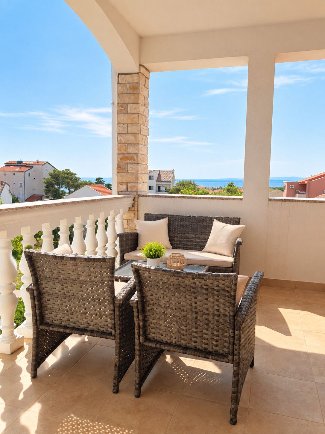 Ein Balkon mit Korbmöbeln, einer Steinsäule und Blick auf das Meer.