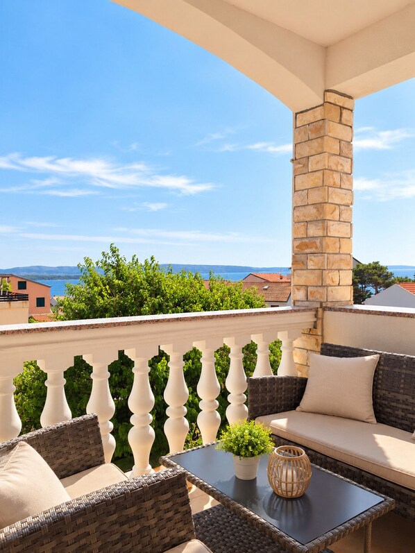 Ein Balkon mit Korbmöbeln, einer Steinsäule und Meerblick.