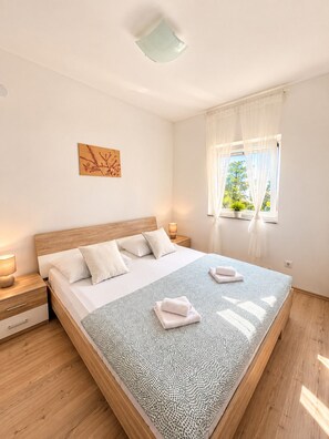 A bedroom with a bed, bedside tables, a window with curtains, and a wall-mounted artwork. - Apartment Bodulo 6 (Povljana)