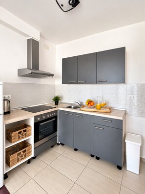 A modern kitchen with grey cabinets, a black stove, and a stainless steel sink.