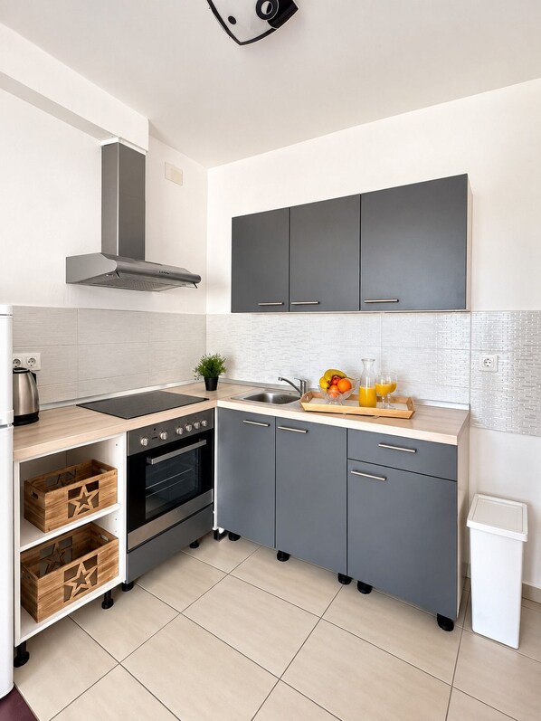 A modern kitchen with grey cabinets, a black stove, and a stainless steel sink.