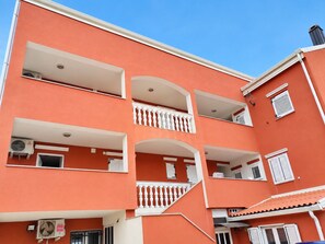 A multi-story building with balconies, air conditioning units, and a tiled roof. - Apartment Bodulo 6 (Povljana)