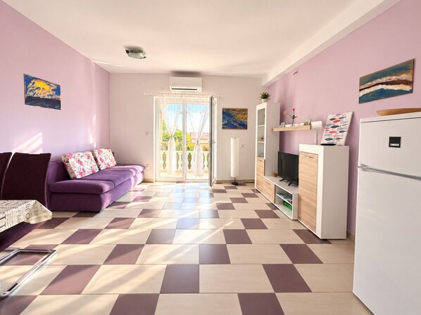 A modern living room with a purple sofa, a flat-screen TV, and a white refrigerator.