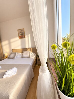 A hotel room with a bed, a bedside table, a nightstand, a window with a view, and a potted plant.