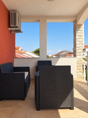 A balcony with wicker furniture, an air conditioning unit, and a view of buildings.