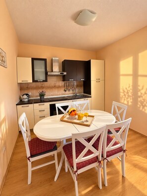 A compact kitchen with modern appliances, a dining table with four chairs, and a breakfast tray with fruit and juice.