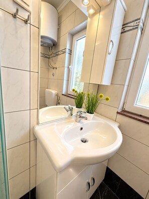 A bathroom with a white sink, two cabinets, a mirror, and a window.