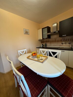 Cozinha compacta com armários brancos, bancada preta e mesa de jantar com cadeiras vermelhas estofadas.