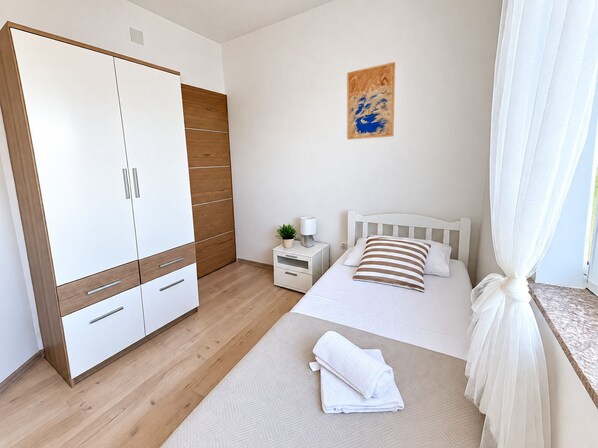 A bedroom with a bed, a wardrobe, a bedside table with a lamp, and a painting on the wall.