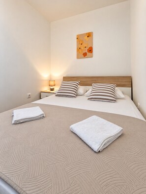Una cama bien hecha con almohadas a rayas, una obra de arte en la pared y una lámpara de noche.